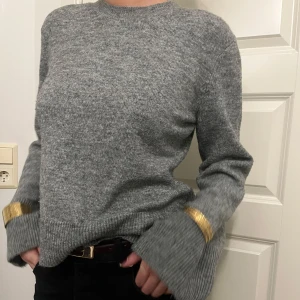 Grå stickad tröja med lite flare armar - Snygg grå stickad tröja med detalj i ärmarna. Perfekt för att ge din outfit en touch av bekvämlighet. Tröjan har långa ärmar och en bekväm passform.