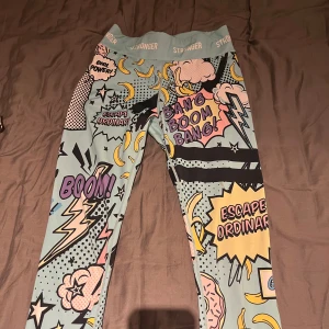 Träningsbyxor från Stronger - Snygga och färgglada träningsbyxor från Stronger med serietidningsinspirerat mönster. De har text som 'Bang Boom Bang!' och 'Girl Power!' i olika färger.  Perfekta för att sticka ut på gymmet eller i vardagen. Inga defekter alls, använt ich 3 gånger. Dom finns inte längre på hemsidan!🩷.             nypris: 800kr. Skriv för frågor💙 storlek S men passar både som Xs och M skulle jag säga. 