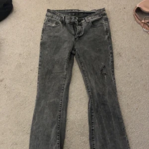 Grå bootcut jeans - Lågmidjade jeans, Snygga grå bootcut jeans med en sliten look. De har en klassisk femficksdesign och en liten reva på ena benet för en trendig touch. Perfekta för en avslappnad stil.