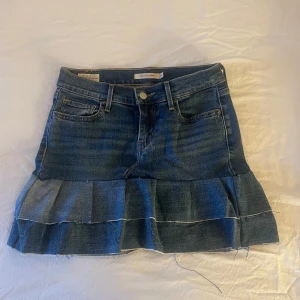 Jeanskjol med volang från Levi's - Snygg jeanskjol från Levi's med volangdetalj i nederkant. Kjolen har en klassisk femficksdesign och är i en mörkblå denimfärg. Perfekt för en avslappnad stil. Jag har sytt den själv. Passar xs-s