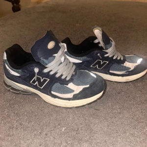 New Balance 2002r - Snygga New Balance 2002r i blått och grått med klassisk snörning. Skorna har en robust sula och är perfekta för vardagsbruk. De har en stilren design med märkets logga på sidan.