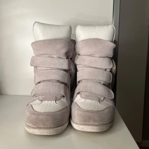 Bekett vita sneakers från Isabel Marant - Snygga vita sneakers från Isabel Marant i mocka och skinn. De är i superfint skick och mycket varsamt använda! Detta är en unikare och exklusiv modell med vit sula istället för den klassiska bruna! Skriv vid frågor! Skulle säga att de är mindre i storleken eftersom att de har en klack, alltså bekvämare att ha större storlek än vanligtvis! Brukar ha 39 1/2 & 40 och dessa har passat mig bra! Dessa kostade 6900, de vanliga brukar kosta 5900!
