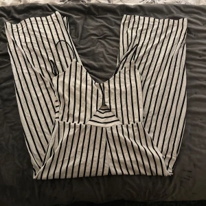 Randig klänning från Stradivarius - Snygg ärmlös byxdress från Stradivarius i svart och vitt randigt mönster. Perfekt för en stilren look med smala axelband och en figurnära passform. (Dom är kortare i benen men ska vara så)