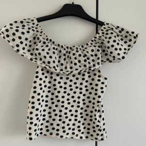 Prickig offshoulder topp - Säljer en söt offshoulder topp med svartvita prickar. Toppen har en volangdetalj runt axlarna som ger en lekfull look. Perfekt för sommarens varma dagar. Passar bra till både jeans och kjol.