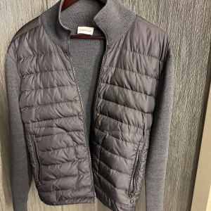 Moncler Cardigan - Snygg grå jacka från Moncler med quiltad framsida och stickade ärmar. Jackan har en dragkedja framtill och ribbad krage. Perfekt för kyligare dagar med sin stilrena design och bekväma passform. bra skick! storlek m passar s