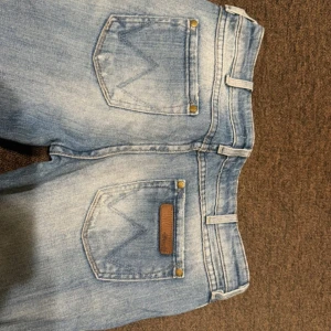 Blå jeans från wrangler - Snygga ljusblå jeans från wrangler med slitna detaljer och låg midja. Köpte på vinted men passade ej. W28/L34, midjemåtten ungefär 37-38cm, innerbenslängd ungefär 80cm💕
