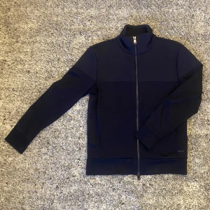 Mörkblå tröja med dragkedja från BOSS - Säljer en stilren mörkblå tröja från BOSS med dragkedja. Tröjan har en hög krage och är långärmad, perfekt för kyligare dagar. Den är tillverkad i ett ordentligt tjockt tyg som ger en snygg passform. 2199:- nypris. Om du önskar ytterligare info eller specifika bilder så är det bara att skriva 🙏