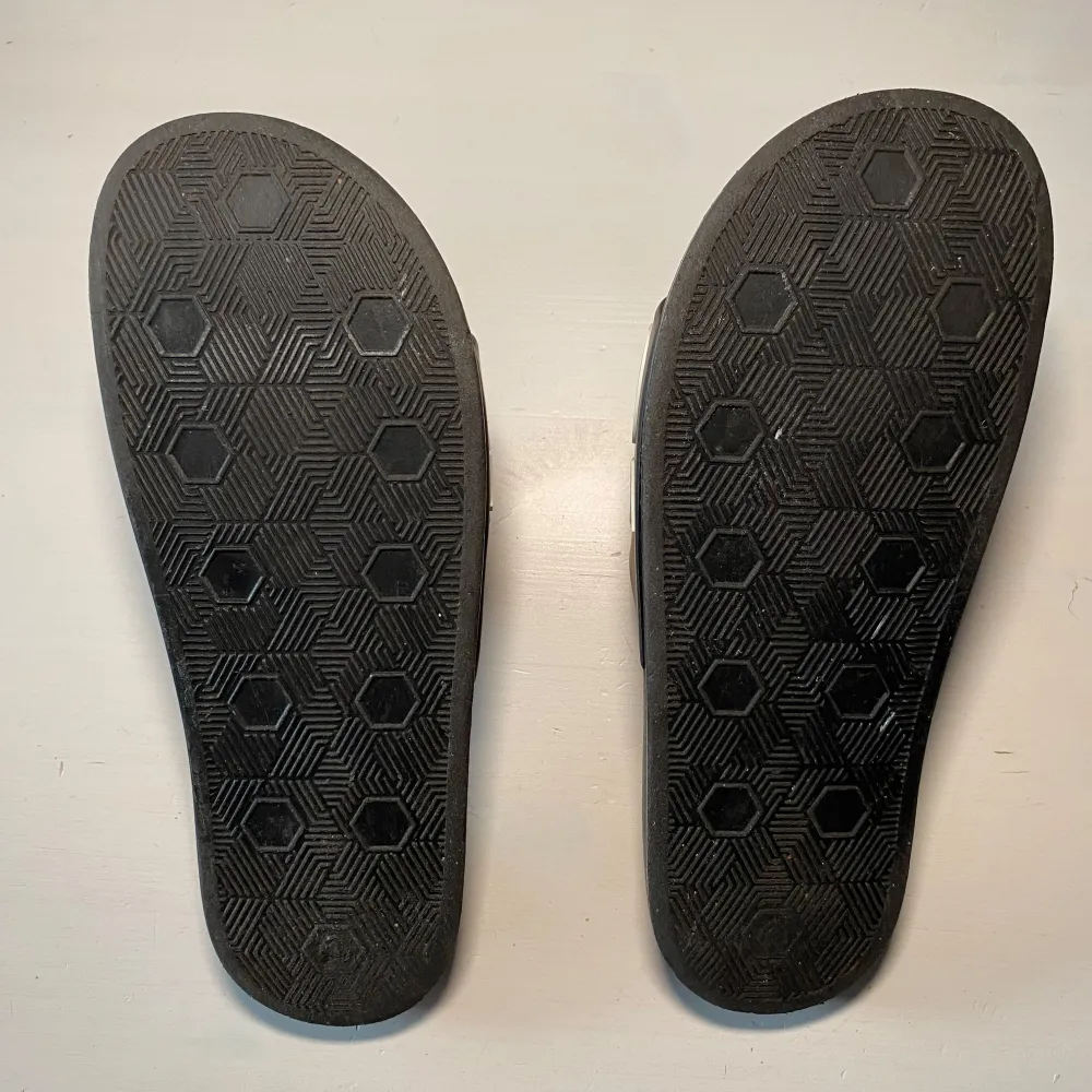 Snygga svarta sandaler med vit text på ovandelen. Sandalerna har en bekväm sula med mönstrad undersida för bra grepp. Perfekta för en avslappnad stil. Jag har storlek 43 och dom sitter lita tajt på mig. Jag gissar att dom är storlek 41-42. . Kengät.