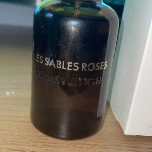 Les Sables Roses Eau de Parfum från Louis Vuitton - Exklusiv parfym Les Sables Roses från Louis Vuitton i en elegant mörk flaska. Flaskan rymmer 100 ml och har en stilren design med märkets logotyp på korken. Perfekt för den som söker en lyxig doftupplevelse.
