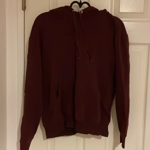 Vinröd hoodie - Säljer en vinröd hoodie med långa ärmar och justerbar huva. Perfekt för en avslappnad stil. Den har en klassisk design med en stor ficka framtill.