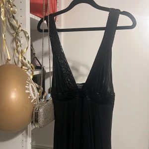 Svart långklänning från Class roberto cavalli - Elegant svart långklänning från Class Rpberto Cavalli med djup v-ringning och glittriga detaljer på axelbanden och midjan. Perfekt för en glamorös kväll. Klänningen har en flytande passform och är tillverkad i ett mjukt, glänsande material. Ny, str 36