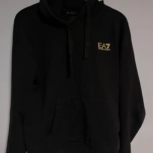 Ea7 hoodie - Tjabba!  Säljer min svarta Emporio armani hoodie då jag vuxit ur den. Det är en tunnare tröja som passar utmärkt till sommarkvällar och höstens klimat! Den har klarat sig från att bli urtvättad o solblekt men det är däremot tyvärr ett hål vid fickan.