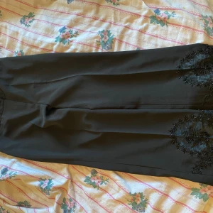 Kostymbyxor y2k - Säljer ett par eleganta svarta byxor med snygga broderade detaljer på benen. De har en klassisk passform och är perfekta för både vardag och fest. Byxorna är gjorda i ett mjukt och bekvämt material som ger en lyxig känsla. Pris kan diskuteras 💗
