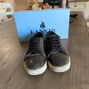 Säljer ett par bruna sneakers från Lanvin. De har en snygg kombination av mocka och skinn med snörning framtill. Skorna har en vit sula som ger en cool kontrast till det bruna. Perfekta för en avslappnad men stilren look.