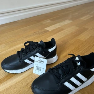 Helt nya svarta Adidas Forest Grove J sneakers - Svarta Adidas sneakers. Helt nya med etikett.  Storlek 38, mindre i storlek. Passar 37.