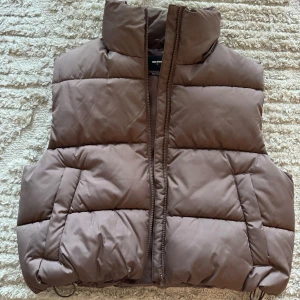 Brun dunväst från Bik Bok - Säljer en snygg brun dunväst från Bik Bok i storlek S. Västen är quiltad och har en dragkedja framtill. Perfekt för höst och vinter, och den är gjord av återvunnet material. 
