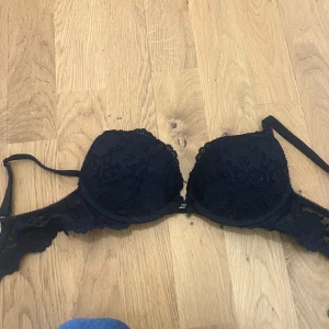 Svart spets-bh - Säljer en svart bh med spetsdetaljer från Cubus. Den har ett litet ”B” framtill och justerbara axelband. Storlek 65b passar även 70a. Lite push i sig! Säljer då den inte passar. Knappt använd, lappen är tyvärr avklippt.