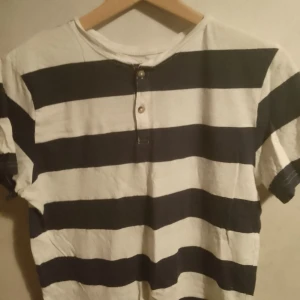 Randig t-shirt från H&M - Säljer en snygg randig t-shirt från H&M i blå och vit. Den har korta ärmar och två knappar vid halsen. Säljer på grund av att jag har ingen användning för den längre