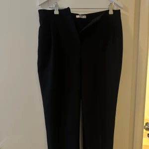 Svarta kostymbyxor från NA-KD - Säljer ett par stilrena svarta kostymbyxor från NA-KD. De är högmidjade och har en klassisk rak passform. Perfekta för både jobb och festliga tillfällen. Byxorna har en dragkedja framtill och är gjorda i ett bekvämt material som ger en snygg siluett.