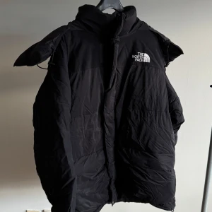 Svart dunjacka från The North Face - Säljer en svart dunjacka från The North Face i storlek L. Jackan är perfekt för kalla vinterdagar med sin tjocka vaddering och långa ärmar. Den har en hög krage för extra värme. Loggan är snyggt broderad på bröstet. 