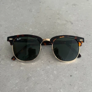 Solglasögon från Ray-Ban - Säljer ett par snygga solglasögon från Ray-Ban. De har en klassisk clubmaster-stil med en sköldpaddsmönstrad båge och guldiga detaljer. Glasen är mörka och ger ett coolt intryck. Perfekta för både sommar och vår!