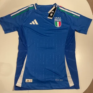 Blå fotbollströja från Adidas - Säljer en snygg blå Italien landslags tröja som representerades i EM. Denna tröja är tillverkad med svettabsorberande AEROREADY som håller dig torr och bekväm både på planen och på läktaren.