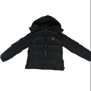 Svart pufferjacka från Trapstar - Säljer en svart pufferjacka från Trapstar med huva och dragkedja. Jackan har ett coolt märke på bröstet och broderad logga på ryggen. Perfekt för att hålla sig varm och stilren under kyliga dagar.