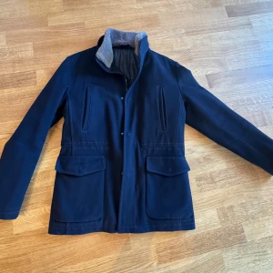 Rose & Born Loro piana jacka  - Snygg mörkblå jacka i Loro piana tyg från Rose & Born, tillverkad i Italien. Jackan har en quiltad insida och är gjord av 100% ull. Den har långa ärmar och stängs med knappar och dragkedja. Perfekt för kyligare dagar med stil. Nypris 20 000kr Öppen till pris förslag