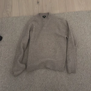 Beige stickad tröja från Uniqlo - Säljer en stilren beige stickad tröja från Uniqlo. Tröjan har en klassisk rund hals och långa ärmar med ribbade muddar. Perfekt för kyligare dagar och enkel att matcha med olika outfits.