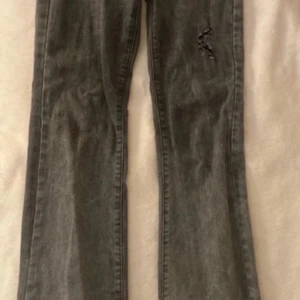 Grå jeansbyxor från Shein - Snygga grå jeansbyxor från Shein i storlek XS. Byxorna har en bootcut-stil och är tillverkade i denim. Perfekta för en avslappnad look med en sliten detalj på ena benet.