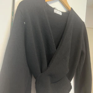 Svart omlottkofta - Snygg svart omlottkofta med knytband i midjan. Den har långa ärmar och är perfekt för en stilren look. Passar bra till både vardag och mer uppklädda tillfällen.