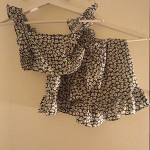 Blommig offshoulder topp shein  - Säljer en söt blommig offshoulder topp med volangdetaljer. Toppen har ett svart och vitt blommönster och är perfekt för sommarens varma dagar. Den har en knytning vid axeln för extra stil. Pris kan diskuteras