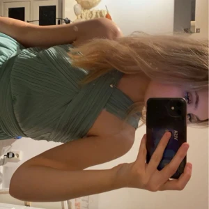 Grön klänning med korsad hals - Elegant grön klänning med korsad halsdesign och plisserad kjol. Perfekt för bal! Endast använd 1 gång.