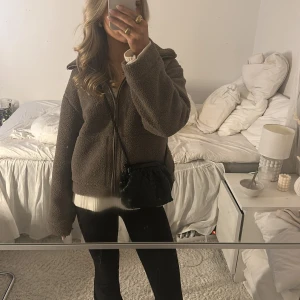 Brun teddyjacka med dragkedja - Mysig brun teddyjacka med dragkedja framtill. Jackan har en hög krage och långa ärmar, perfekt för kyligare dagar. Den har en avslappnad passform och är gjord i ett mjukt teddy-material.