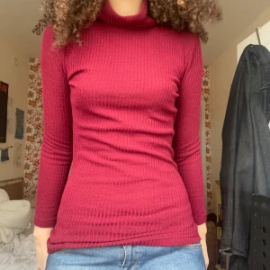 Vinröd ribbad polotröja - Snygg vinröd polotröja med ribbad struktur. Perfekt för kyligare dagar med sin långa ärmar och sköna passform.