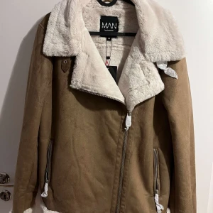 Brun jacka med vit fuskpäls från boohoo - Säljer en snygg brun jacka från boohoo med vit fuskpäls på kragen och insidan. Jackan har dragkedja och två fickor med dragkedjor. Perfekt för kyliga dagar med sin mysiga och stilrena design. Storlek M.