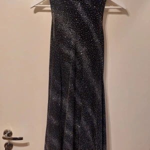 Svart glittrig klänning - Snygg svart klänning med glittrigt mönster.. Den är ärmlös och har en elegant passform. Mycket mjuk och bekväm. Strl M.