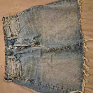 Blå jeanskjol från Brema - Snygg blå jeanskjol från Brema med fransig nederkant och klassisk femficksdesign. Kjolen har en knappgylf och är perfekt för en avslappnad stil. Den är tillverkad i slitstarkt denim och har en bekväm passform.