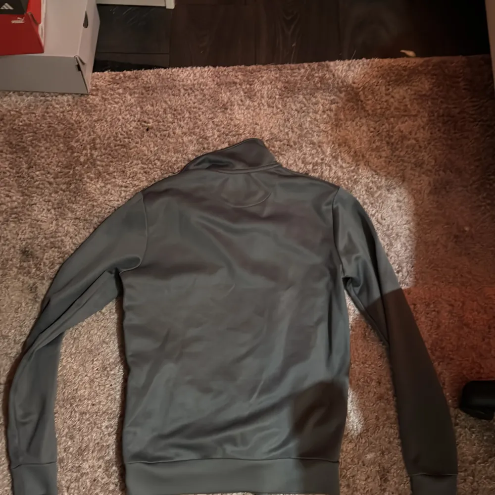 Säljer en grå tröja från Lyle & Scott med dragkedja och två vita ränder över bröstet. Tröjan har en avslappnad passform och långa ärmar. Perfekt för en stilren och bekväm look.. Neuletakit & Villapaidat.