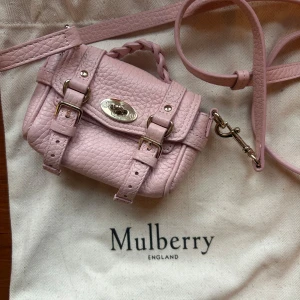 Rosa axelväska från Mulberry - Säljer en söt rosa axelväska från Mulberry i skinn. Väskan har ett flätat handtag och justerbar axelrem. Den är dekorerad med spännen och en snygg metallplatta framtill. Perfekt för att ge din outfit en touch av elegans. Micro storleken, passar att ha kort i. 100% Calf Leather Height 8.5 cm / Width 11 cm / Depth 5 cm / Handle drop 3 cm / Strap drop 52 - 60 cm