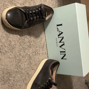 Svarta sneakers från Lanvin - Snygga svarta sneakers från Lanvin med en stilren design. Skorna har en svart ovandel med snörning och en ljus sula. Perfekta för en trendig look.