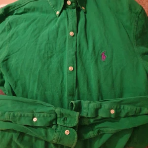 Grön långärmad skjorta från Ralph Lauren - Snygg grön långärmad skjorta från Ralph Lauren i featherweight mesh. Skjortan har knappar och en broderad logga på bröstet. Perfekt för en stilren look.