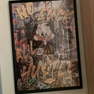 Tavla med tecknad figur och text - En färgglad tavla med en tecknad figur i centrum och texten 'NO LUCK ALL HUSTLE' i stora bokstäver. Tavlan har en svart ram och en livlig bakgrund med olika mönster och färger.