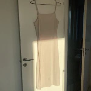 Ljusbeige klänning från H&M - Säljer en ljusbeige klänning från H&M. Den har en smickrande lång design med smala axelband och en  slits på högersidan. Perfekt för en stilren look. 🌸