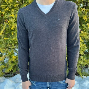 Mörkgrå tröja från Lindeberg - Säljer en stilren mörkgrå tröja från Lindeberg med v-ringning. Tröjan har långa ärmar och en liten broderad logga på bröstet. Perfekt för en avslappnad men snygg look. Man kan även  klä upp den mer, med en snygg skjorta under!