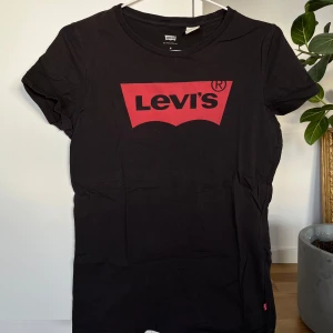 Svart t-shirt från Levi's - Säljer en klassisk svart t-shirt från Levi's med det ikoniska röda logotyptrycket på bröstet. T-shirten är kortärmad och tillverkad i mjuk bomull. Perfekt för en avslappnad stil. 🖤
