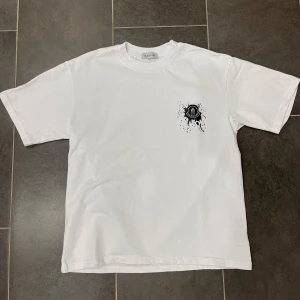 Vit t-shirt från Moncler - Säljer en HELT NY stilren vit t-shirt från Moncler med ett svart tryck på bröstet. T-shirten har en klassisk passform och korta ärmar. Perfekt för en avslappnad look. Tröjan är alltså ALDRIG använd