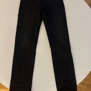 Svarta jeans från Replay - Snygga svarta jeans från Replay med straight high rise fit. De har en klassisk design med knappar framtill och är perfekta för en stilren look. Passar bra till olika outfits och tillfällen.