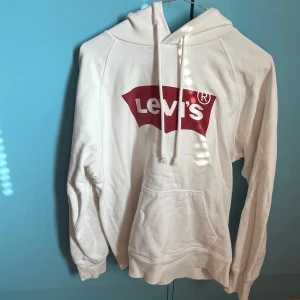 Hoodie från Levi’s - Vit hoodie från Levi’s med rött tryck. Storlek S. Är stor i passformen och lite längre modell.