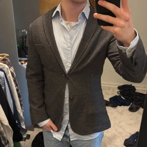 Grå kavaj i ull - Snygg grå kavaj från J.lindeberg i 100% ull. Perfekt för en stilren look med två knappar framtill och fickor. Passar bra till både jeans och mer formella byxor. Ett måste för garderoben! Nypris på denna är runt 2500kr. Skriv vid funderingar!